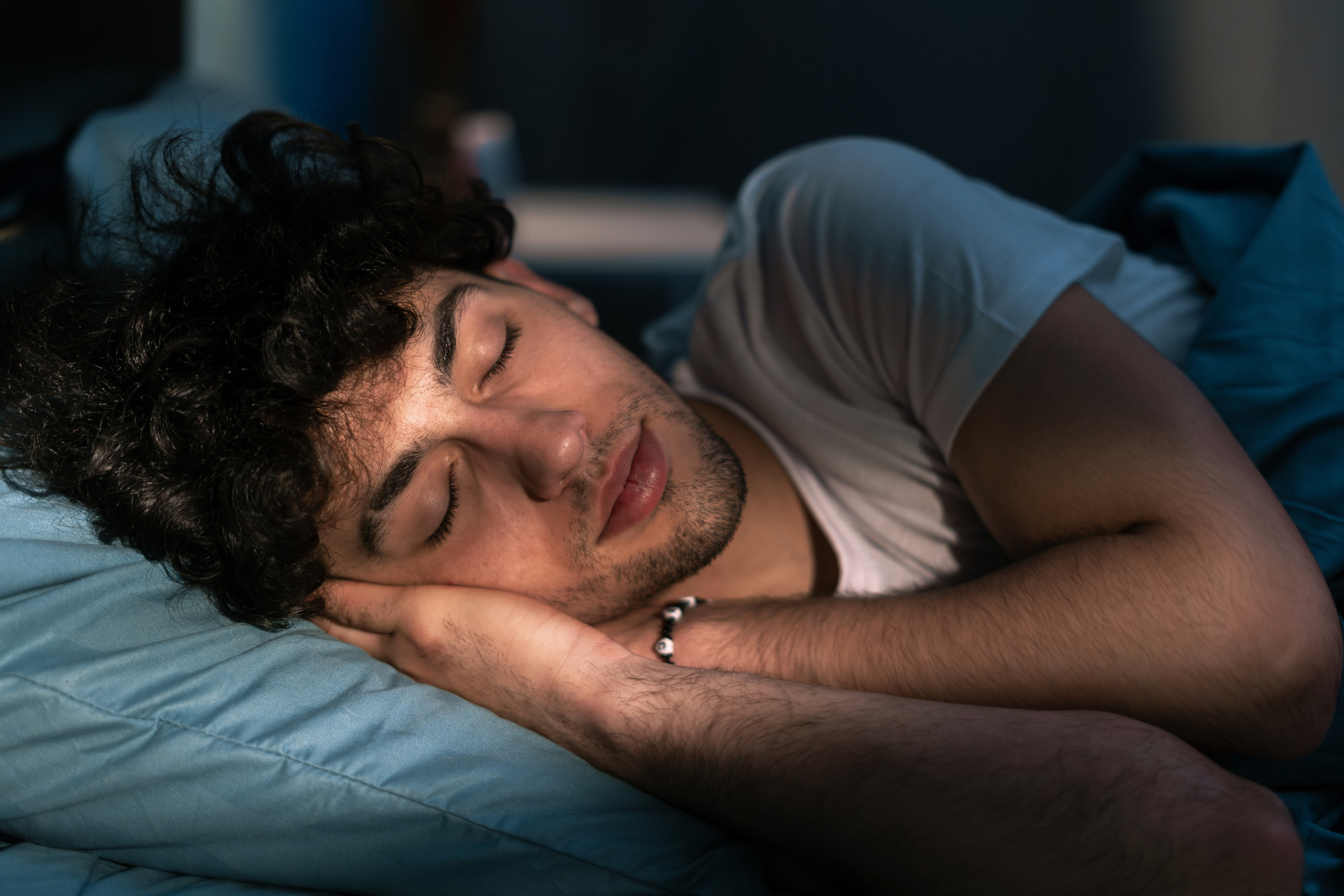 Handsome young man sleeping on pillow in dark room at night, resting at night time. Healthy sleep concept